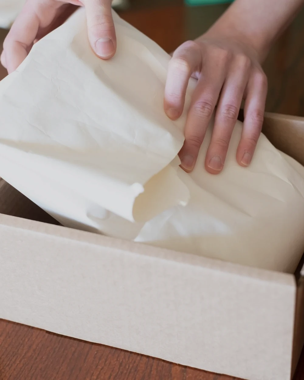 Hands placing protective packing paper inside a clean cardboard shipping box.